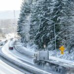 Cars drive on a snowy road, obeying traffic signs and safety expectations