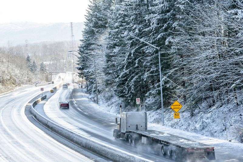 Cars drive on a snowy road, obeying traffic signs and safety expectations