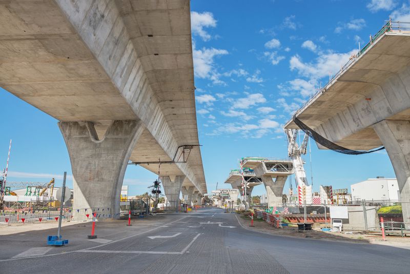 A road under construction and an unfinished overpass with safety barriers, cones, and a blue sky