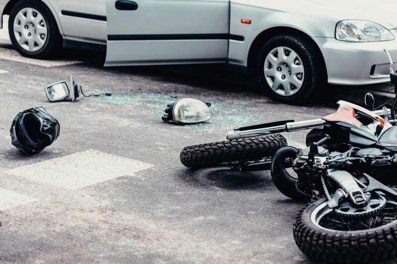 A motorcycle and motorcycle helmet on the ground next to a car