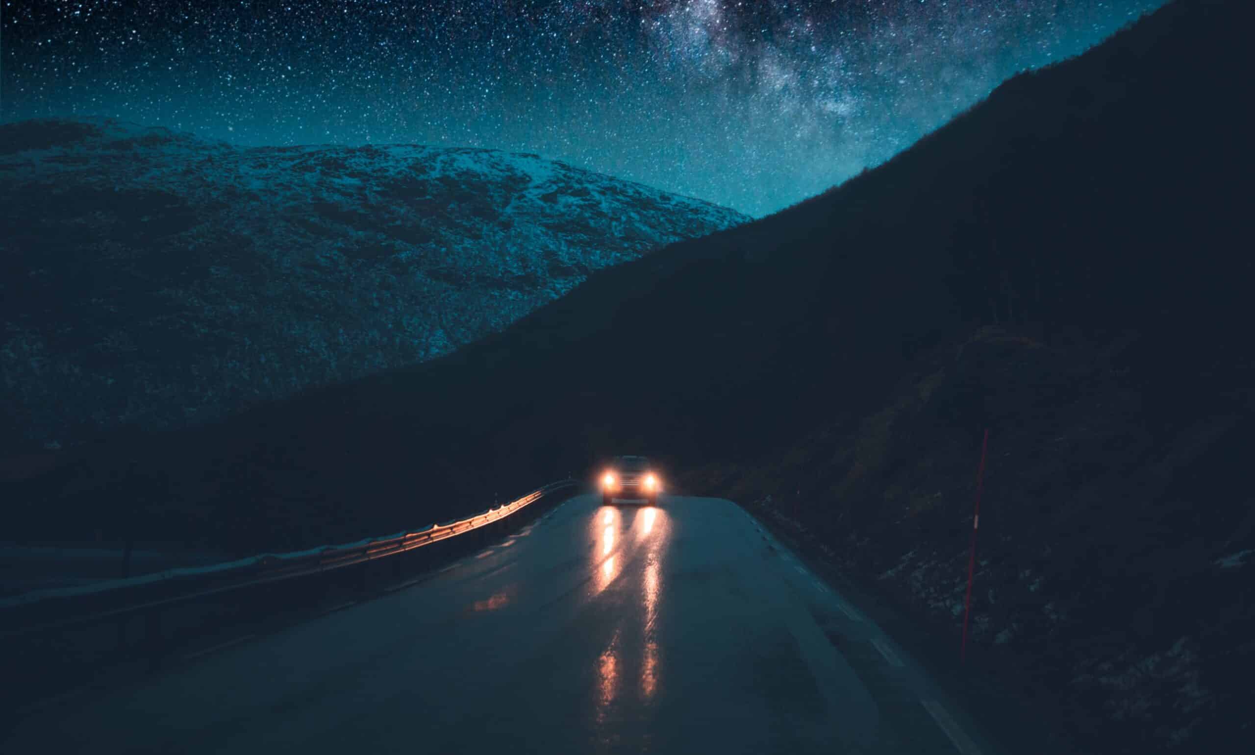 A car driving at night on a mountain road under the stars