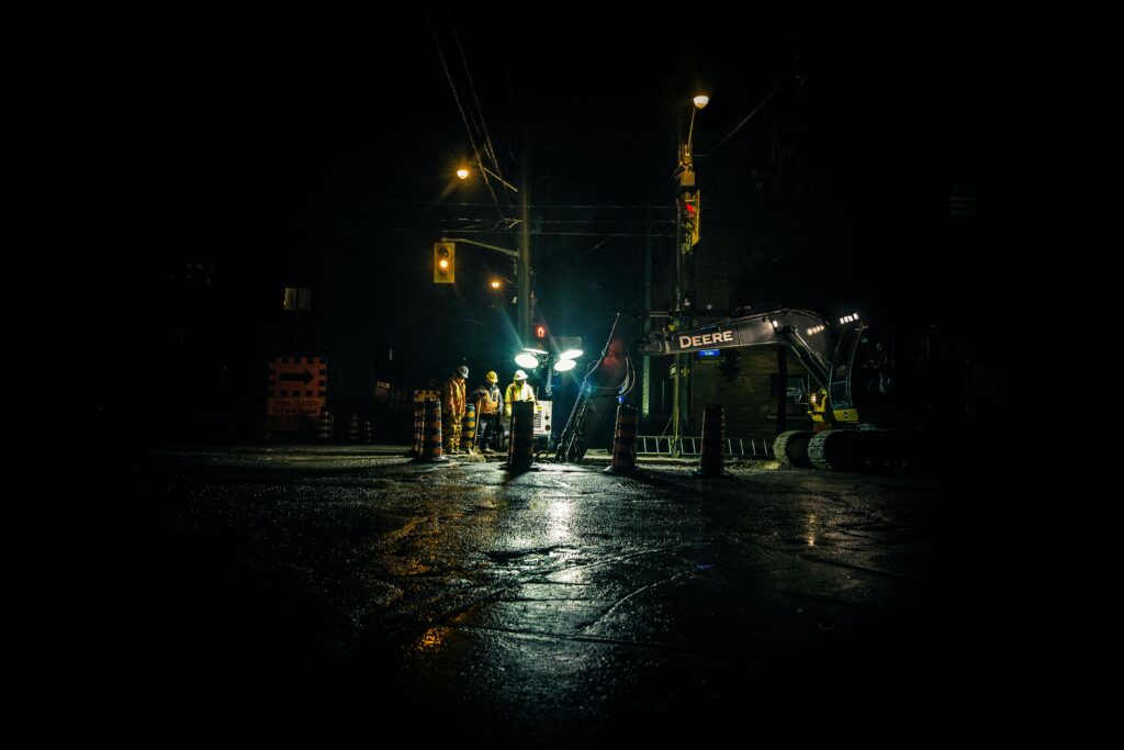 A road work zone at night with workers surrounded by traffic control supplies https://unsplash.com/photos/LKufzuBn8Bs?utm_source=unsplash&utm_medium=referral&utm_content=creditShareLink