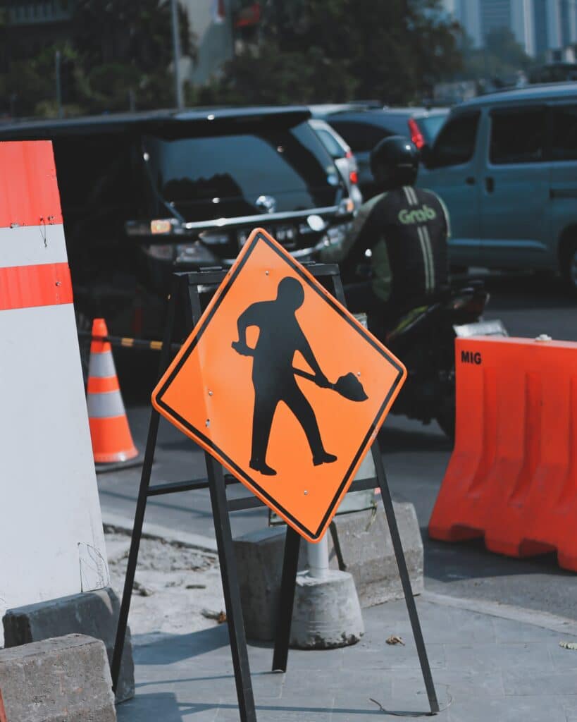A road work ahead sign on the edge of a construction buffer zone. https://unsplash.com/photos/FWbqBav2TsU?utm_source=unsplash&utm_medium=referral&utm_content=creditShareLink