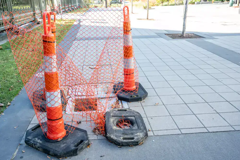 Three Looper Tube types of traffic cones placed around an open hole in a sidewalk area