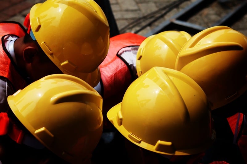 A group of construction workers wearing yellow hard hats, having a meeting