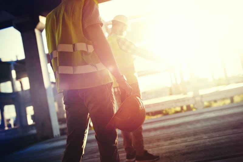 Two construction workers in reflective vests and hard hats at a work site