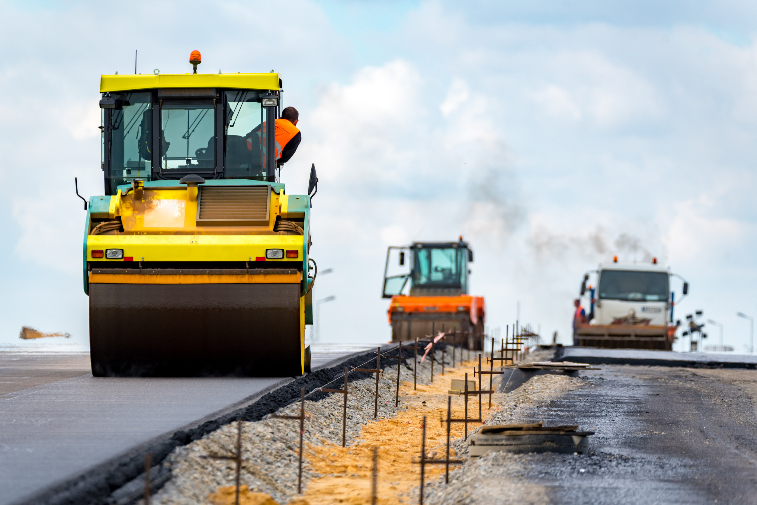 Workers practice roadside construction safety as they pave a new road with heavy machinery