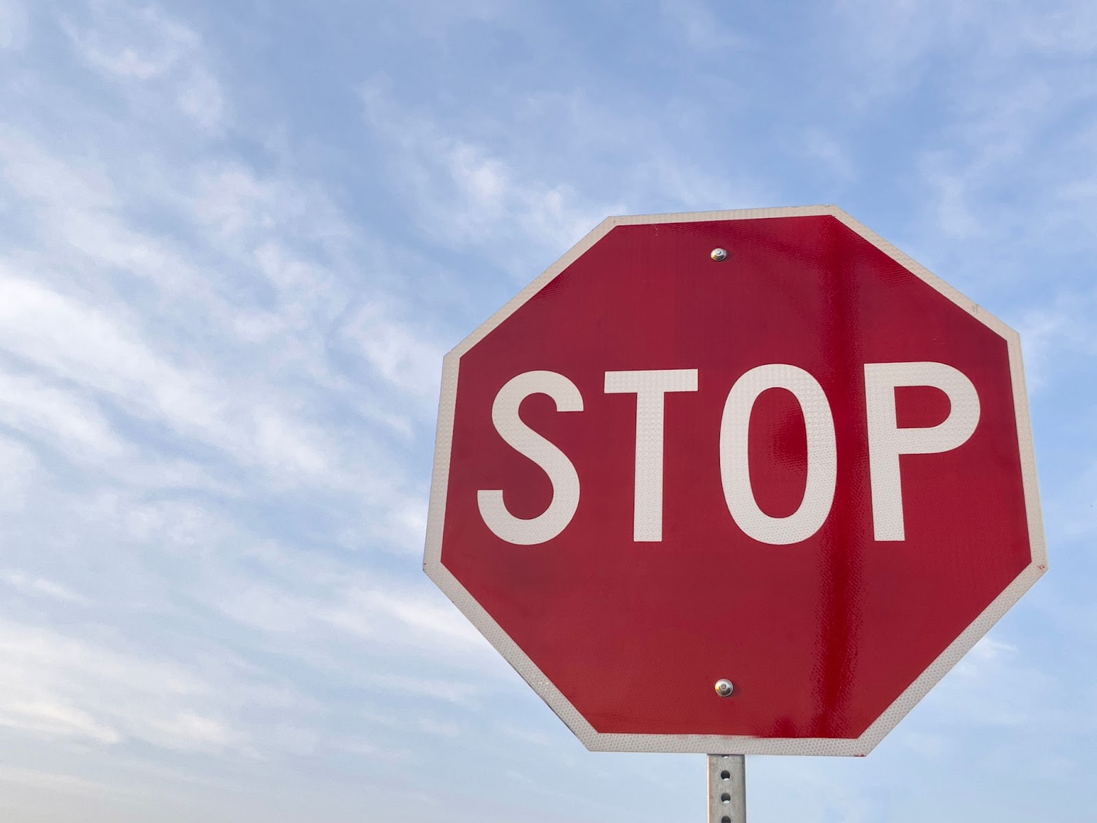 A stop sign attached to a metal breakaway sign post under cloudy skies