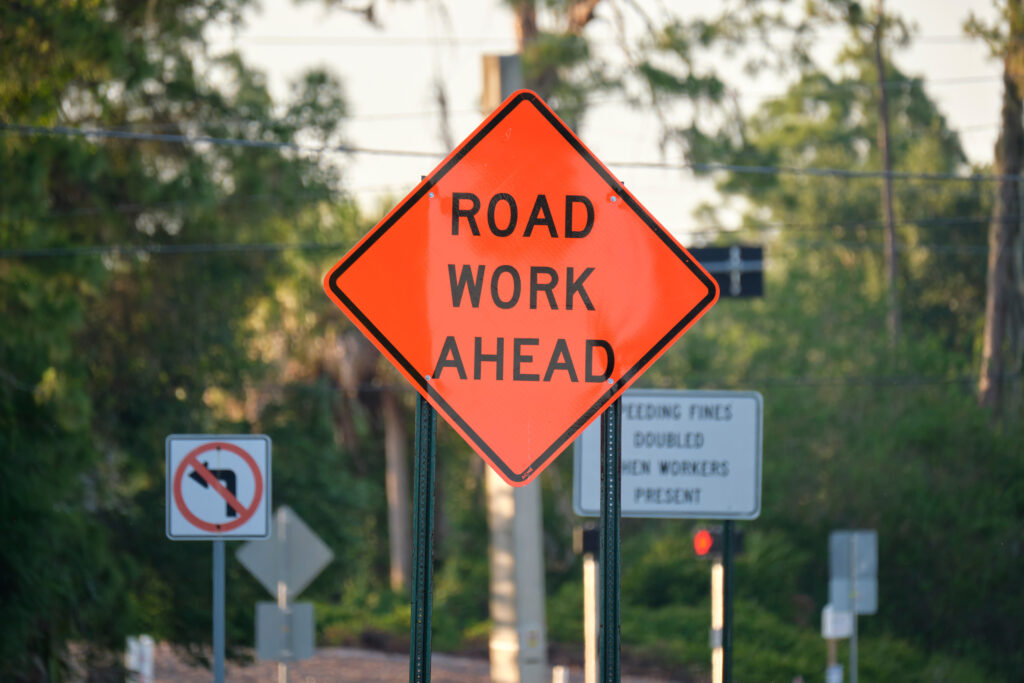 A Road Work Ahead sign in the foreground with other signs in the background